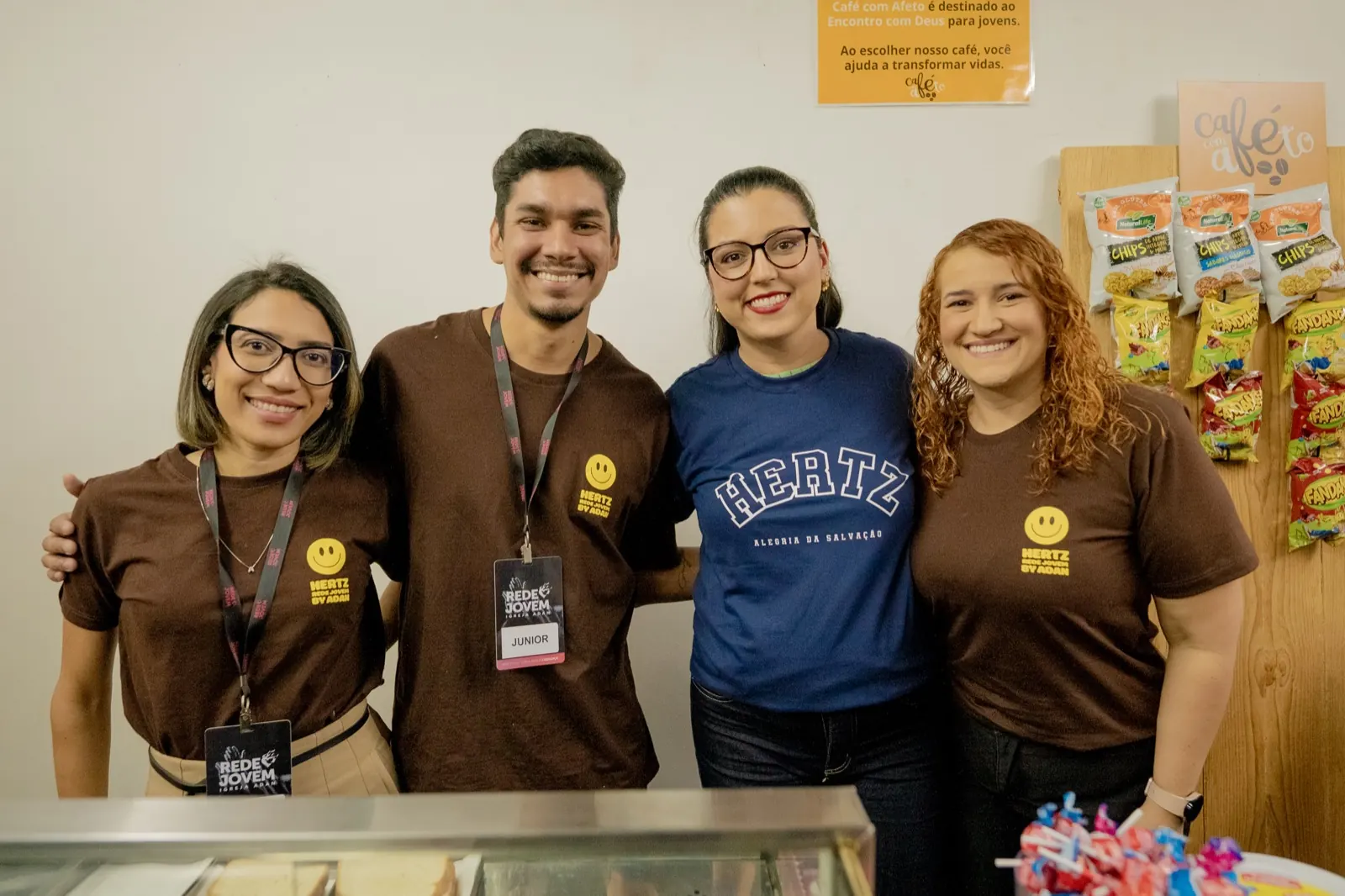Quatro voluntários sorrindo atrás do balcão do Café com Afeto