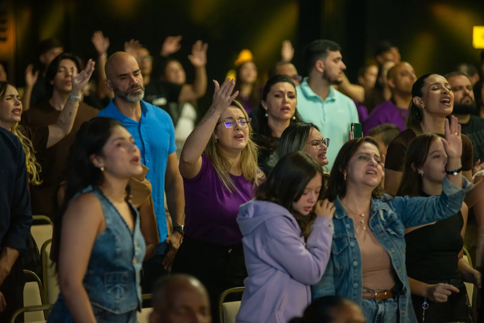 Plateia de mãos erguidas, cantando e orando durante o louvor